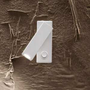 Ideal Lux Page AP Square 142258 - включена лампа върху каменна стена Апликът Ideal Lux Page AP Square 142258 в бял цвят с включена светлина и наклонена глава върху каменна стена