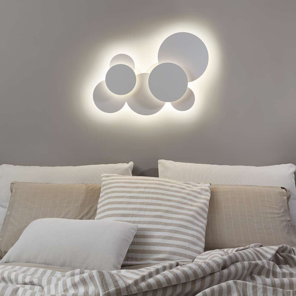 Ideal Lux Cloud PL D74 285207 е монтиран на стена над легло и осветява индиректно пространството около белите кръгли елементи