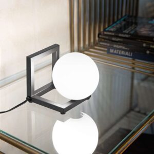 Настолна лампа Ideal Lux Angolo TL1 284316 с черна метална рамка и светеща бяла сфера върху стъклен плот до книги